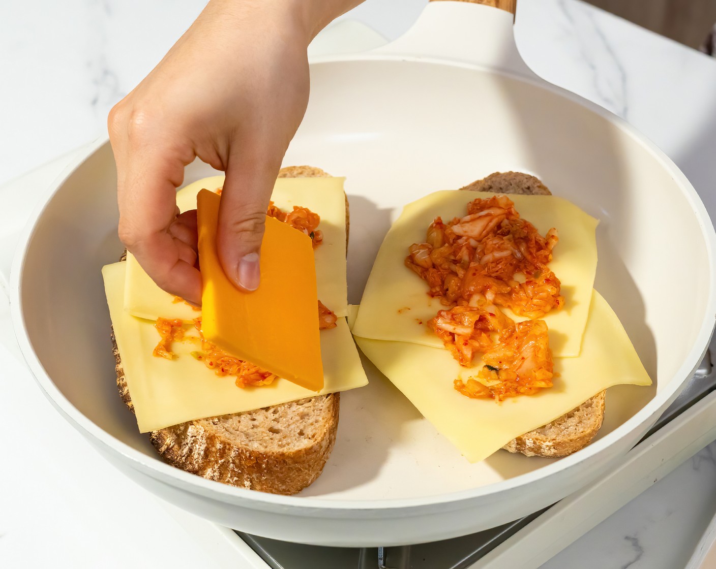 step 2 Heat a large non-stick skillet with a lid over medium heat. Once the pan is hot, place 2 pieces of bread, mayonnaise-side down on the skillet. Top with 2 slices of Gouda (4 slices), 2 Tbsp of Kimchi (4 Tbsp), then 2 American Cheese Slices (4). Put the lid on and cook until the cheese begins to melt and the bottom is golden brown.