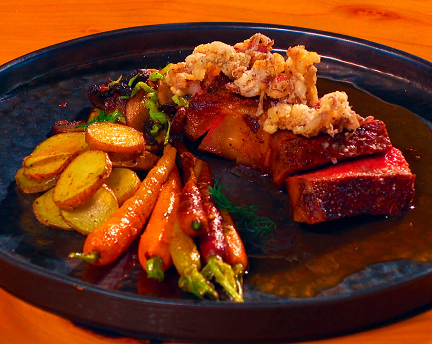 step 15 Assembly: Slice the steak and top with the crispy squid. Plate with the potatoes, carrots, and sauce and garnish with the Fennel Leaves (to taste).