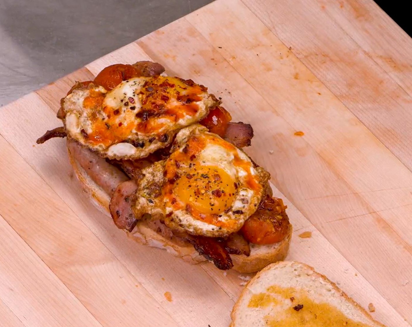 step 3 Assemble: Use a spoon to drizzle the fat from the eggs across the slices of bread. Cut the sausages in half and place on the bread along with the bacon. Drizzle the tomatoes with the Aged Balsamic Vinegar (1 tsp) and place on top of the bacon. Finish the sandwich with the fried eggs and remaining slice of bread.
